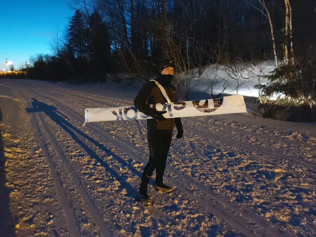 Un fondeur porte son sac Skisäk sur l'épaule au coucher du soleil