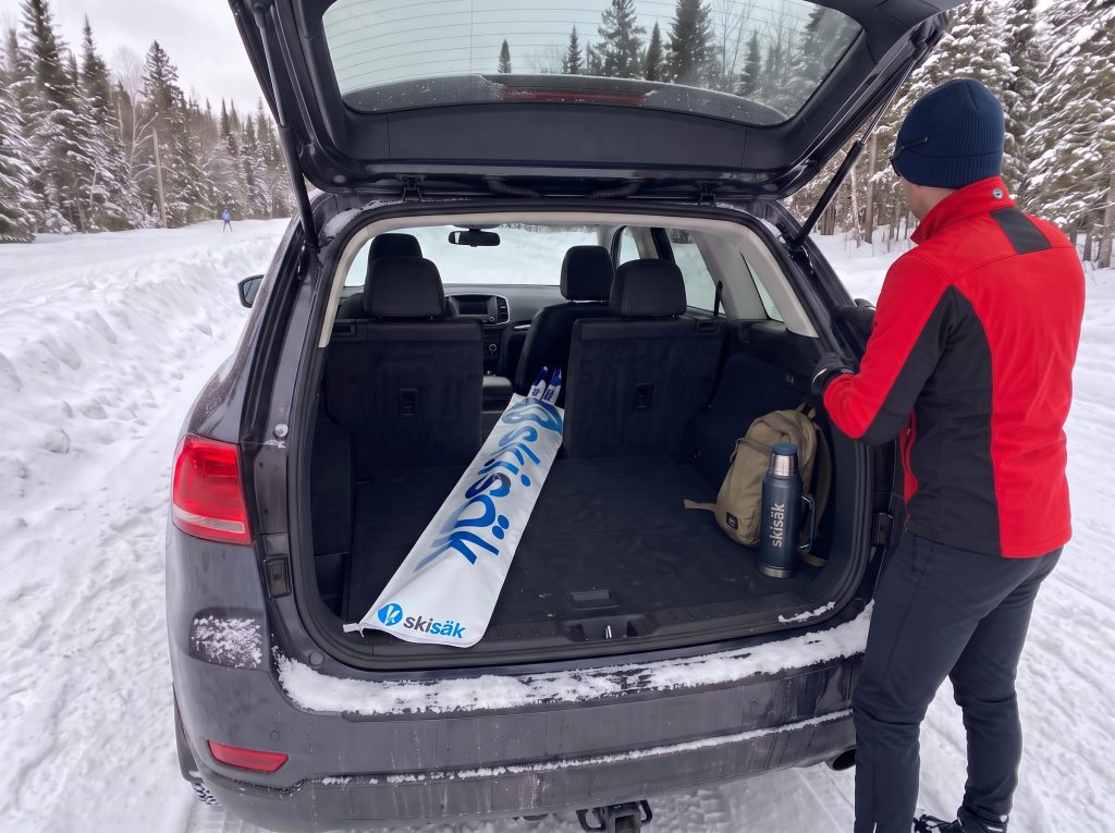 Un fondeur range son sac Skisäk avec ses skis dans le coffre de son VUS, au départ d'un sentier enneigé